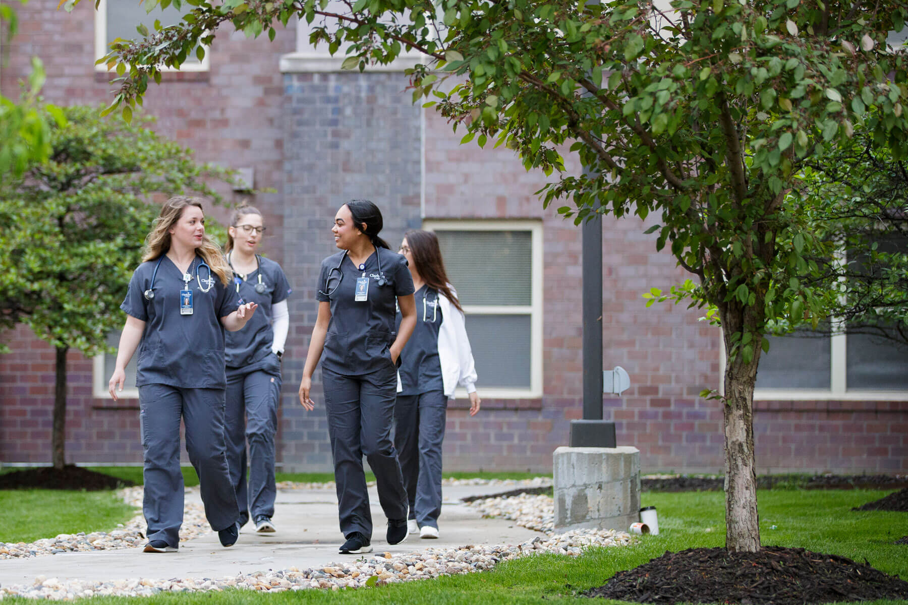 Four women, wearing scrub suits, walking along a sidewalk - Clarkson College students.