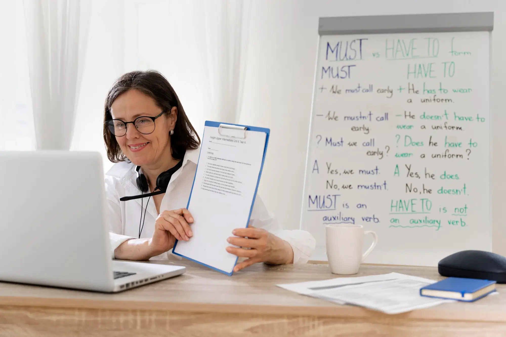 A woman in a white coat sitting at a desk with a laptop, engaged in online learning.