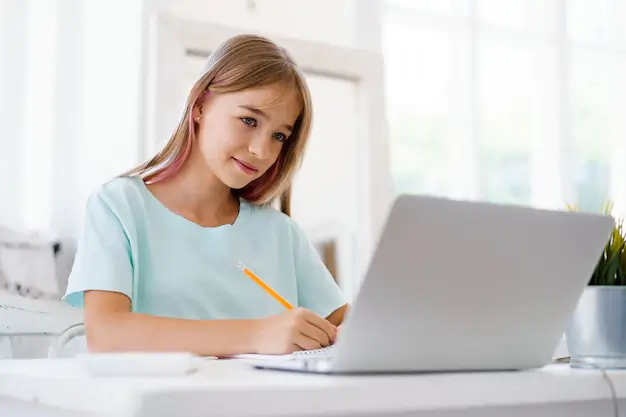 A girl sitting at a desk with a laptop, engaged in online learning.