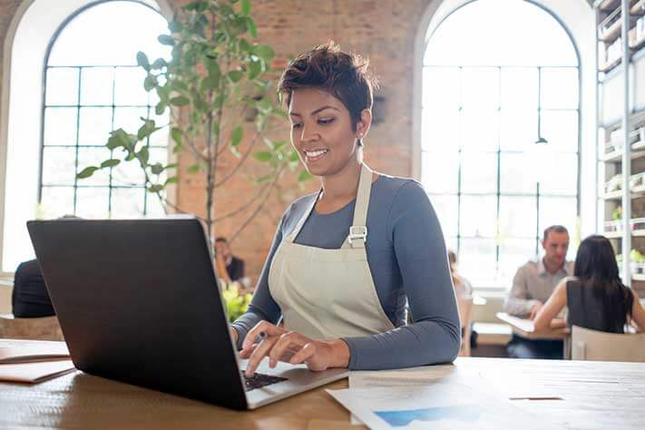 A woman in an apron typing on a laptop.