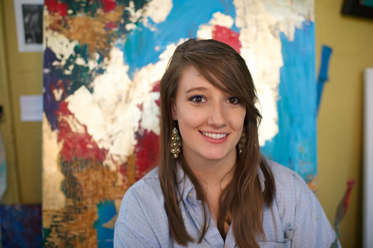 Woman smiling in front of painting in city at night.