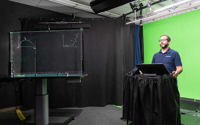 A man standing in front of a green screen with a laptop.