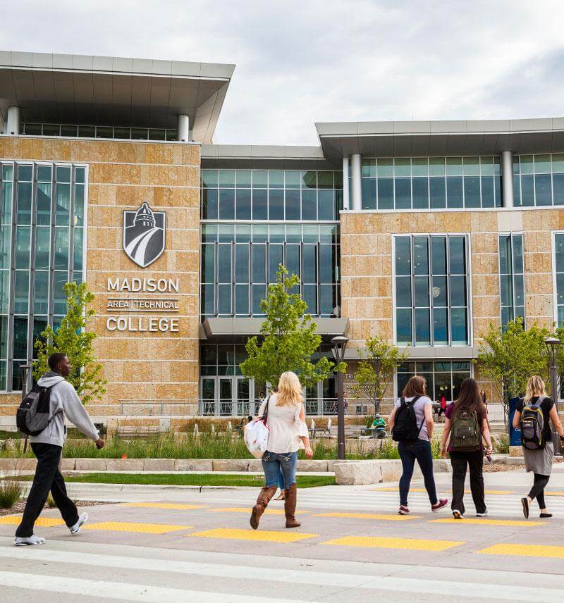 People walking in front of Madison Area Technical College, a large building with a prominent sign.