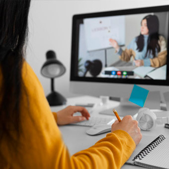 A woman sitting at a desk, using a computer screen and holding a pen to work.