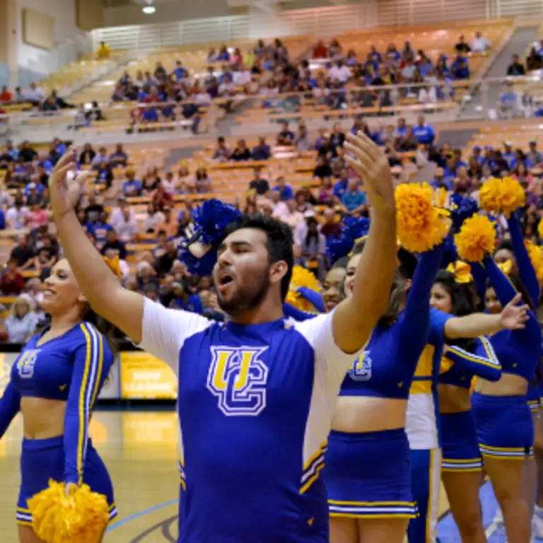 Cheerleaders performing at a basketball game with a lively crowd in the background.